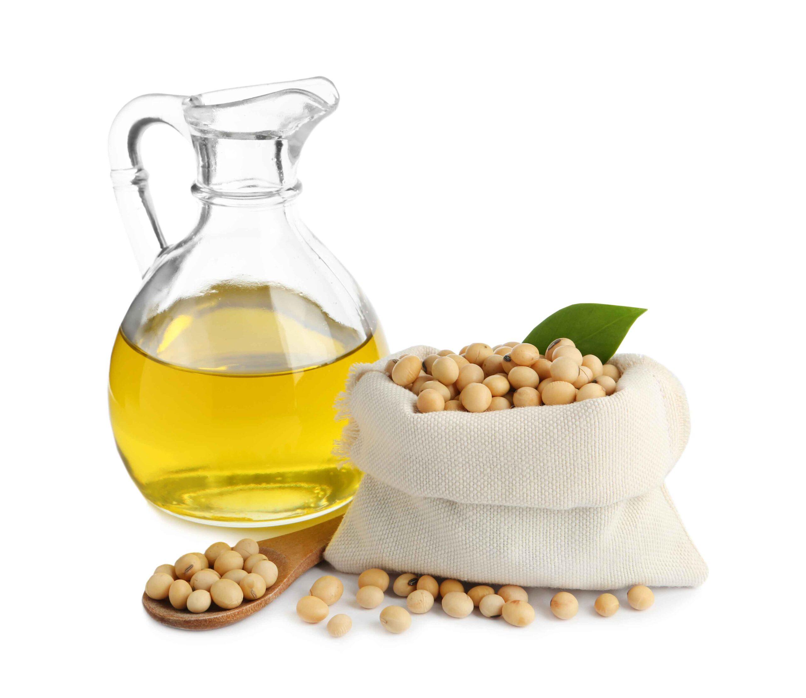 Glass jar of soybean oil with a bag and wooden spoon of soybeans on a white background.