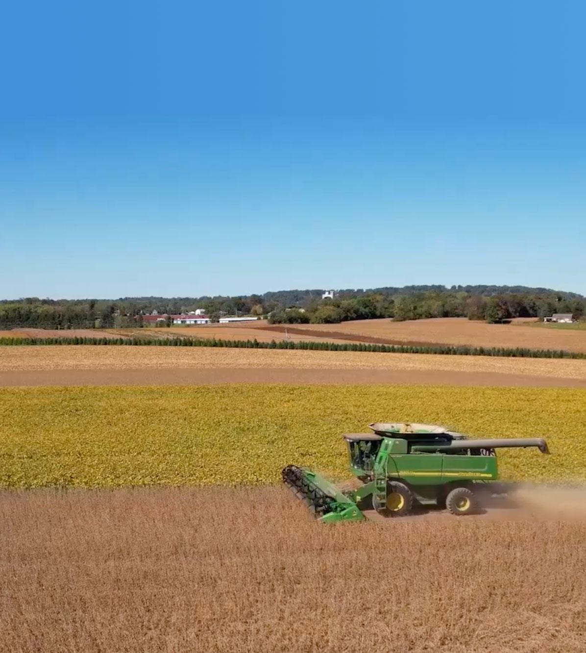 Side view of a green combine harvester reaping crops in a field.