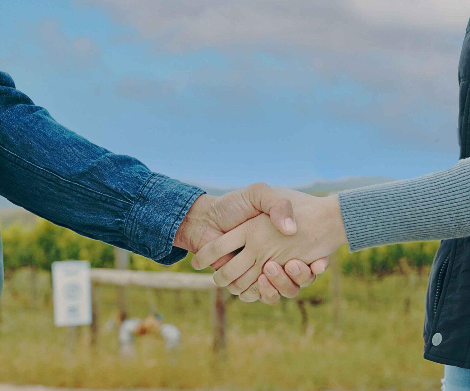 Two hands, one male and one female, shaking with a background of country scenery.