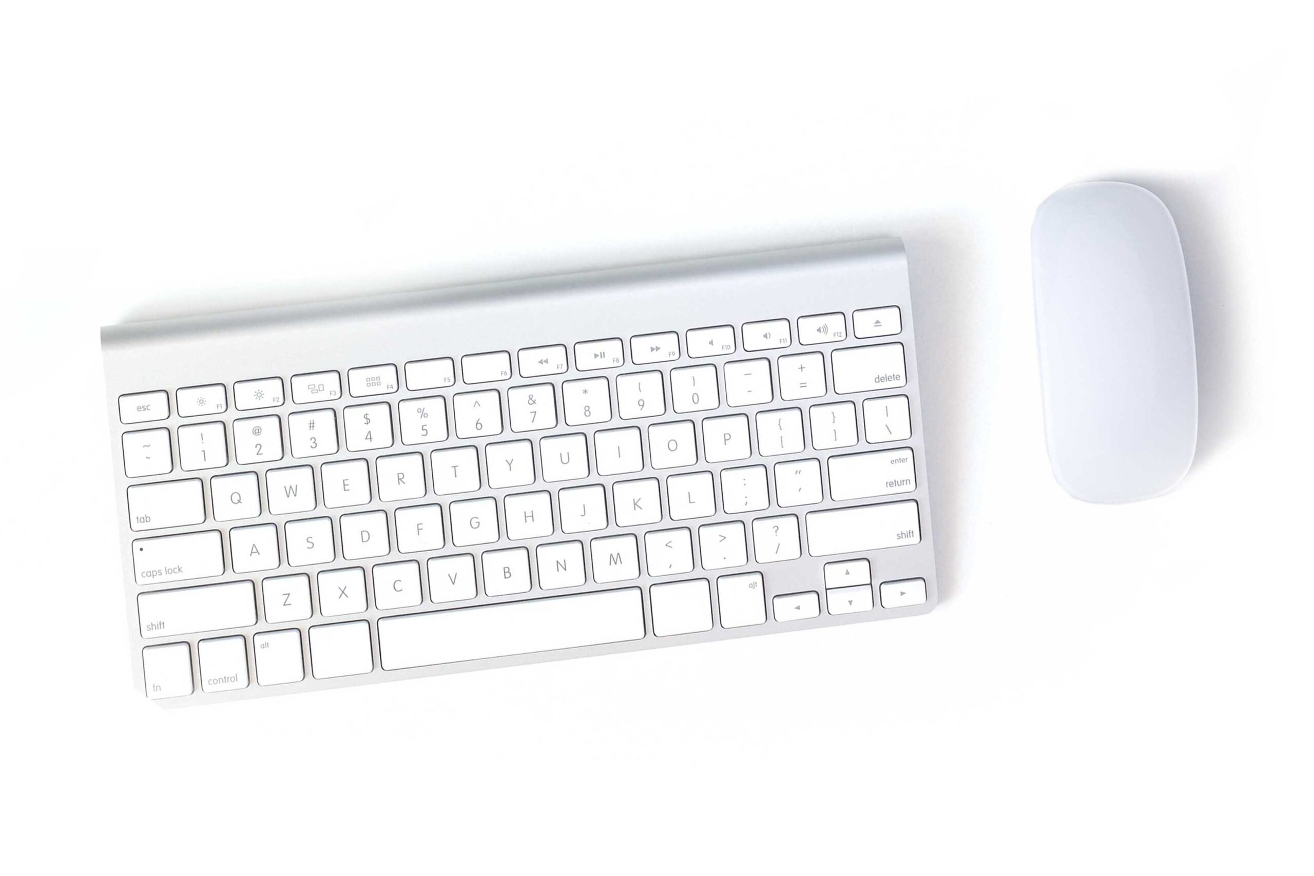 An aerial view of a white keyboard, and white mouse, on a white background.