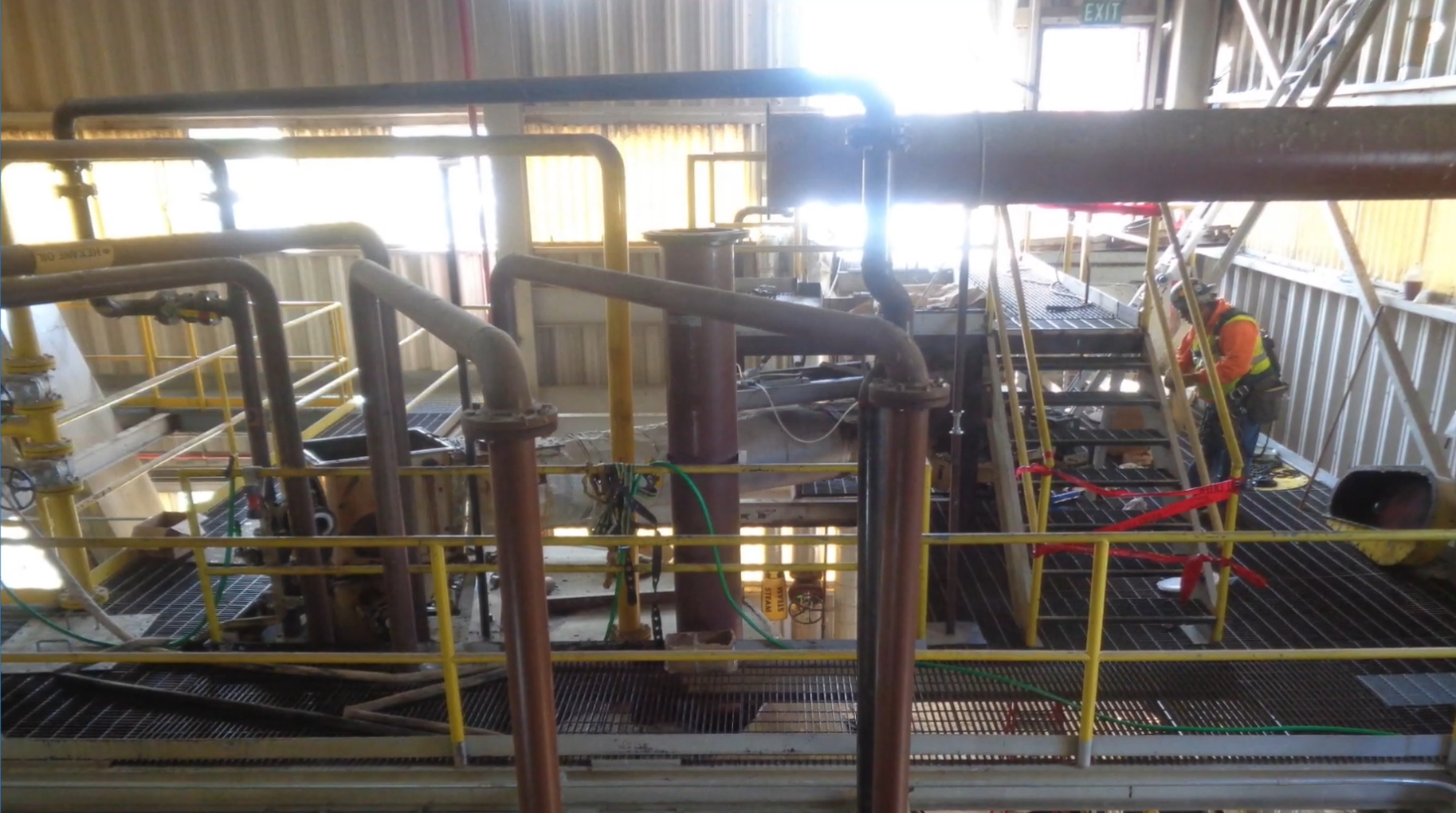 A lot of pipes and grated stairs and walkways inside an oil refinery building.